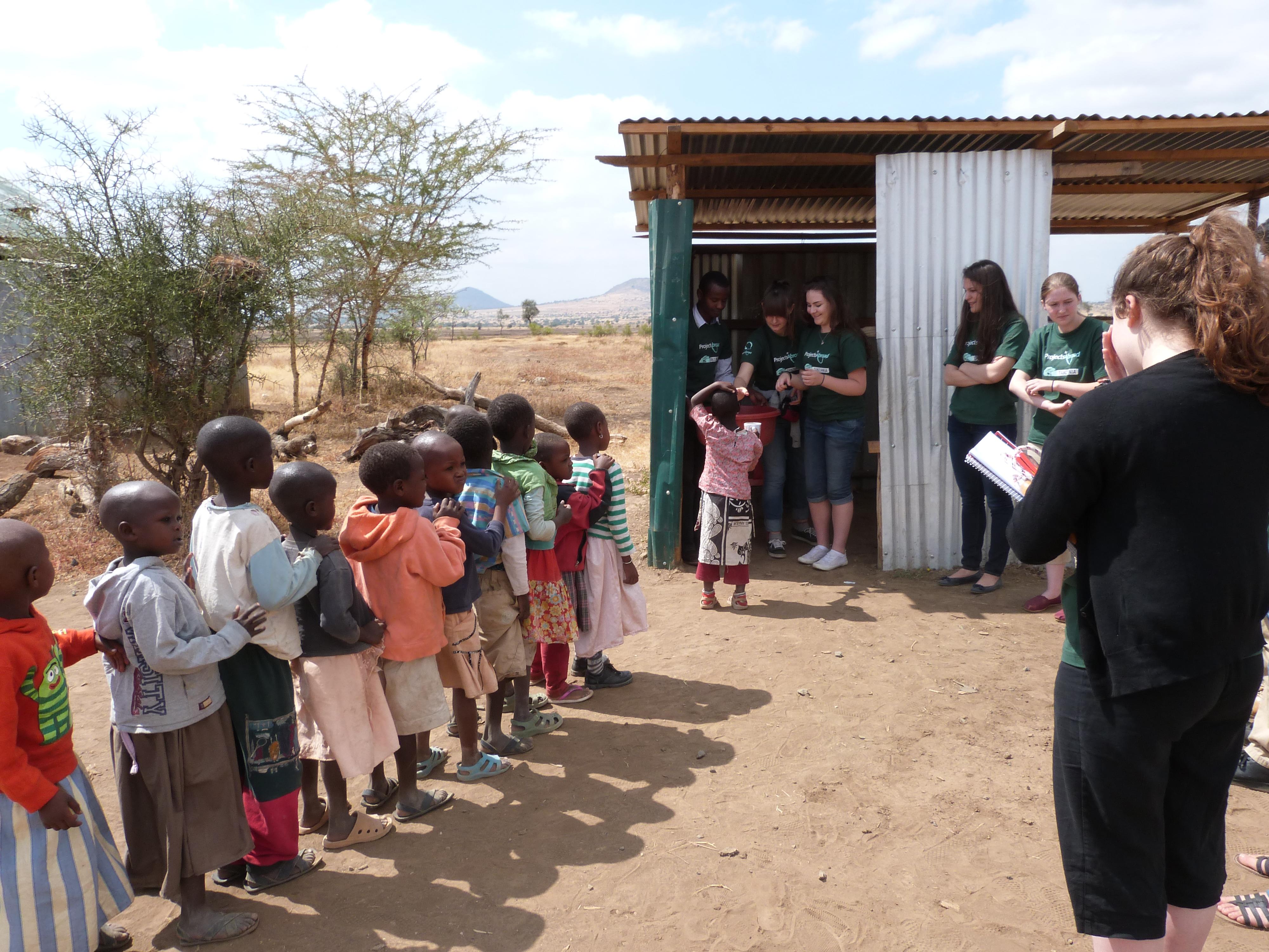 Niños se forman para su revisión de salud durante brigada médica de nuestra pasantía en Tanzania. Pasante revisa a niños durante brigada médica en Tanzania.